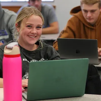 一位坐在笔记本电脑前的学生对着镜头微笑